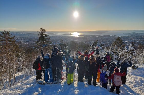 en gruppe mennesker som står på en snødekt ås med trær og solen i bakgrunnen