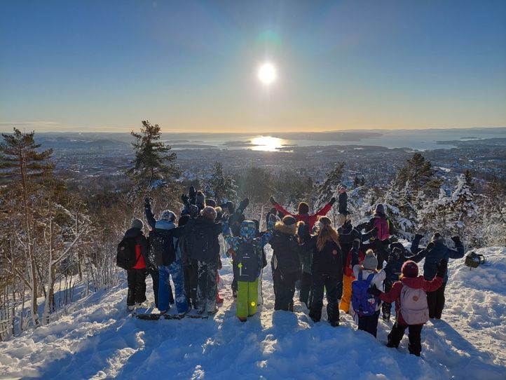 en gruppe mennesker som står på en snødekt ås med trær og solen i bakgrunnen